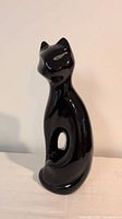 Front left view of glossy black ceramic cat figurine showing pierced body and overall form