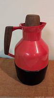 Front view of orange-red carafe showing teak handle and stopper