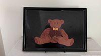 Front view of black tray showing inlaid teddy bear design