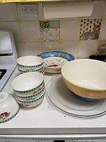 Overall lot showing stack of green-rim bowls, two decorative plates, large mixing bowl, and two glass plates