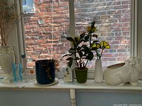 Group shot of all items on windowsill: Lenox vase, ceramic hippo planter, ribbed bud vase, glass wavy-edge vase, blue planter, rectangular planter, faux plant, dried flowers