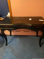 Full view of black writing desk showing three drawers, curved front, cabriole legs