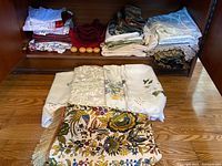 Shelf and floor showing multiple folded linens and napkin rings