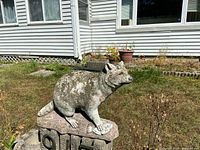 Side view of concrete raccoon statue on stone base situated outdoors
