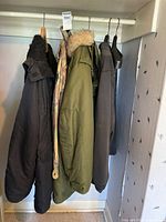 Four jackets on closet rod: black parka, camouflage jacket, olive parka, charcoal coat