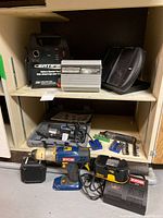 Group shot of all items on shelving showing drill, chargers, rotary tool, inverter, booster pack, solar panel and bits