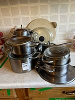 Stacked stainless steel pots, lids, fry pans, pizza pans, pizza stone