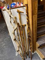 Group of six sticks leaning against wall: two twisted branches, three straight canes, one carved staff