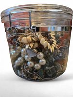 Front view of glass container showing mixed broken jewelry pieces inside