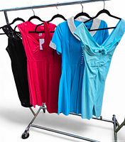 Four of the five dresses on rack: black lace, hot pink tagged, turquoise with white collar, magenta behind