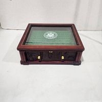 Closed box front view showing carved panel, brass pulls, glass top