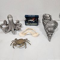 Group shot showing all items: octopus, conch, shark jaw, brass crab, tin of plastic sea animals
