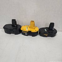 Front view of three battery packs—black DeWalt, yellow DeWalt, black aftermarket—standing upright