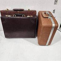 Three suitcases grouped: two brown attachés stacked, tan hardshell alongside