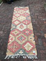 Full view of long runner rug with fringe laid on brick surface