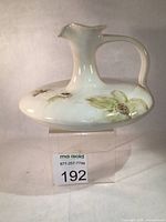 Front view of white stoneware ewer with dogwood relief, handle and spout visible