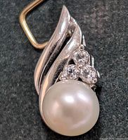 Front close-up of pendant showing pearl, three clear stones and white gold swirl