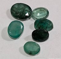 Six loose oval emerald gemstones grouped on white background