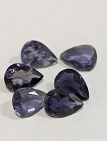 Six pear-cut violet-blue iolite gemstones displayed on white background