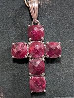 Front view of silver cross pendant showing six dyed ruby stones and bail