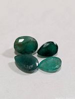 Four green faceted emeralds grouped on white background