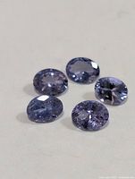 Five loose oval faceted tanzanite gemstones on light background