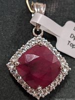 Front view of sterling silver pendant featuring cushion-cut dyed ruby with halo of clear stones