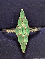 Front view of ring displaying six marquise emeralds and clear accent stones