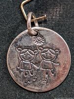 Front view of circular silver pendant showing engraved two children design