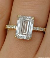 Ring on finger showing emerald-cut center stone and pavé shoulders