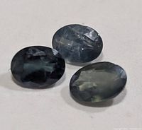 Three oval faceted dark bluish-green alexandrite stones on white background