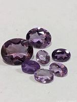 Seven loose faceted purple amethysts displayed