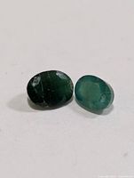 Two oval faceted emerald gemstones on white background