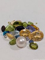 pile of assorted faceted gemstones and pearl on white background