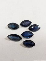 Six marquise-cut dark blue sapphires displayed on neutral background
