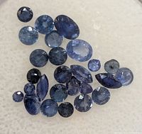 Loose faceted blue sapphire gemstones on white background showing variety of sizes and cuts