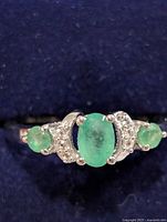 Front view of silver ring showing emerald stones and accent stones