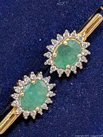 Front view showing oval green stones with CZ halo on blue background