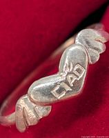 Ring frontal view showing heart, wings and raised lettering detail