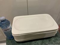 Stack of nine identical white rectangular trays beside 500 ml water bottle for scale