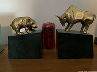 Front view of brass bear and bull bookends with soda can for scale