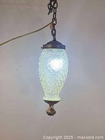 Full view of illuminated pressed glass pendant lamp with chain