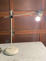 Full view of lamp showing base, vertical stem, horizontal arm and lit shade