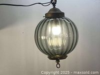 Full view of illuminated ribbed smoke glass globe lamp with cord and top cap visible