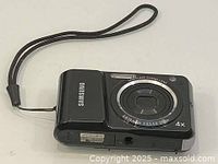 Front view of Samsung ES25 digital camera showing lens, flash, and wrist strap