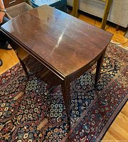 Three-quarter view of mahogany drop-leaf table showing grain, leaves down, tapered inlaid legs