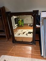 Front view of antique oak framed mirror standing on floor, shows stepped corners, beveled glass and patina.
