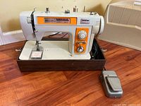 Front view of Brother sewing machine on woodgrain base with foot pedal and case beside