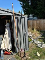 Full view of pole saw, pole pruner and leaf rake leaning against shed