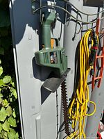 Hedge trimmer mounted on wall with yellow cord and hanger hooks